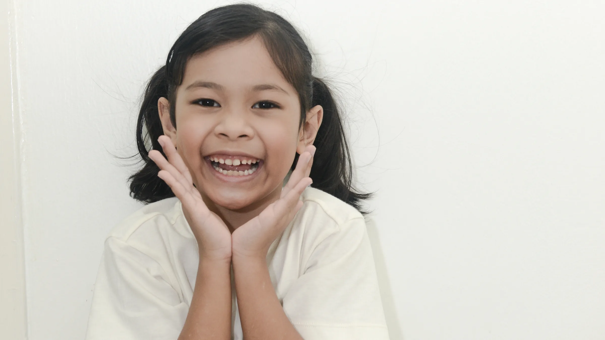 A little girl beaming with both hands cupped against her cheeks